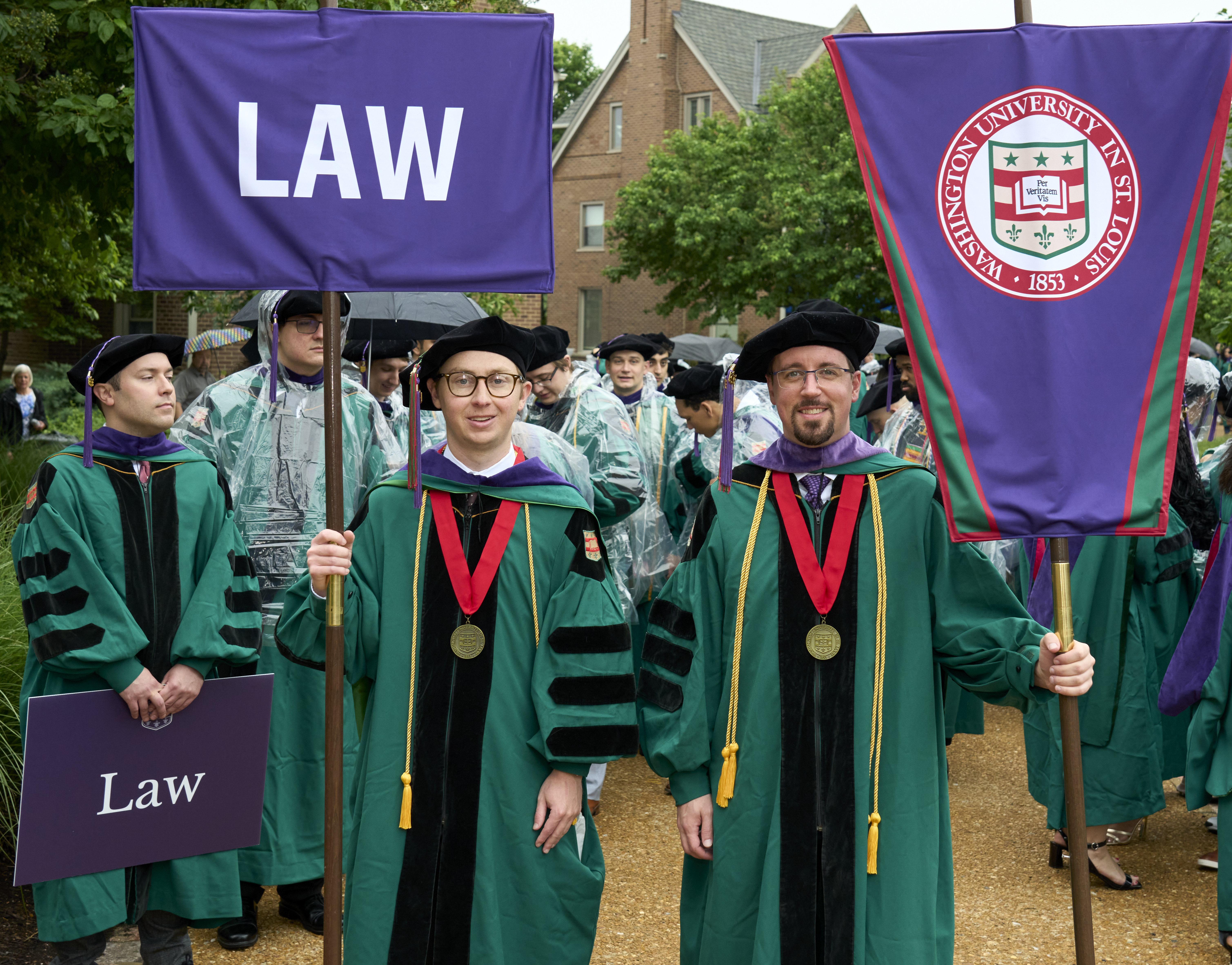 Gavin McGimpsey and another student dressed in academic regalia and holding processional banners.