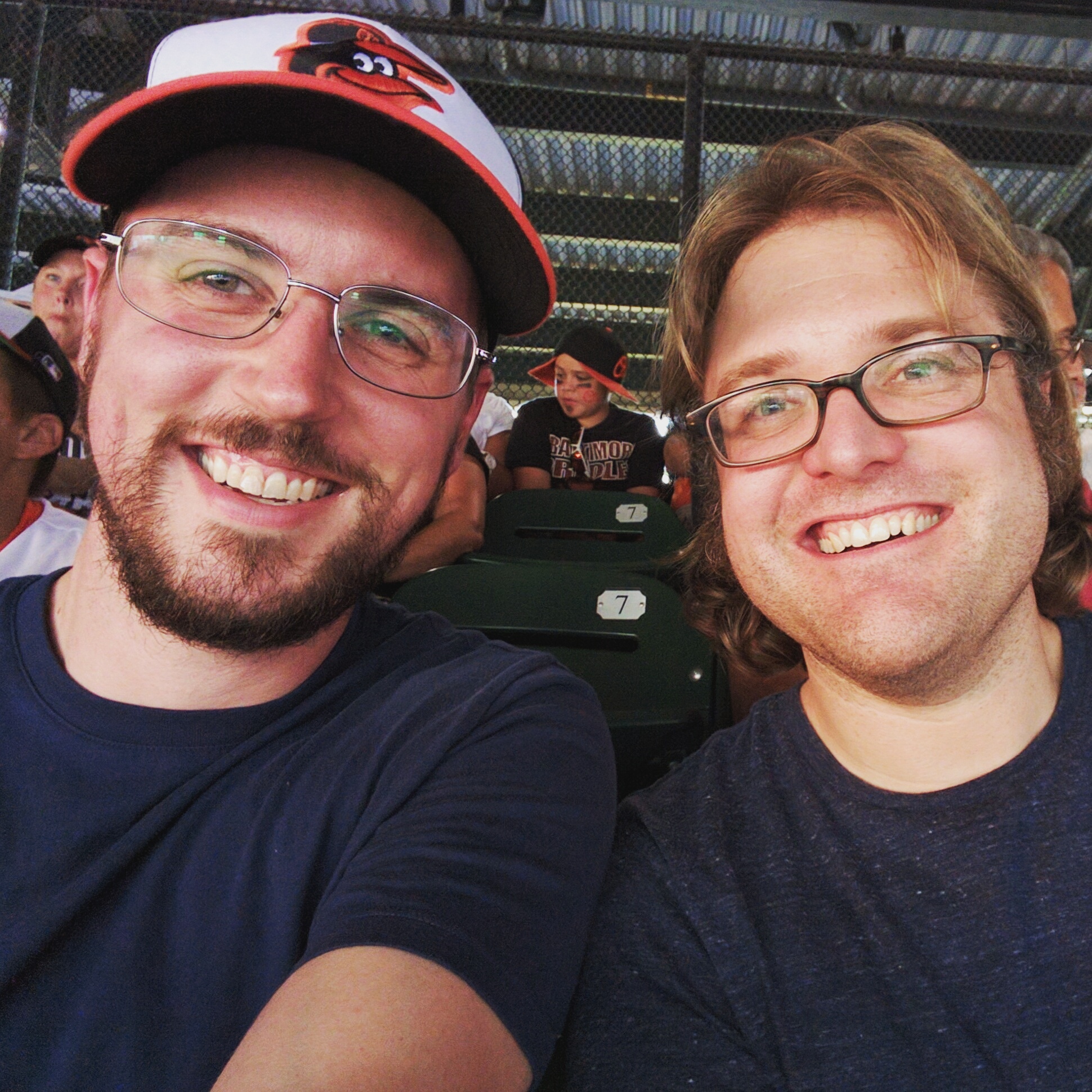 Photo of Gavin McGimpsey and a friend at Oriole Park in Camden Yards. Gavin is wearing an Orioles baseball cap.